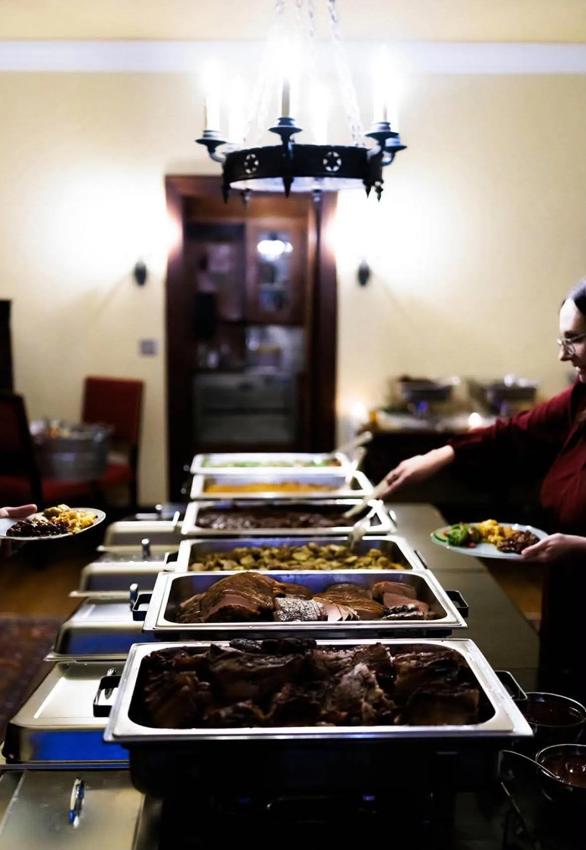 A guest serving food from a row of buffet trays.