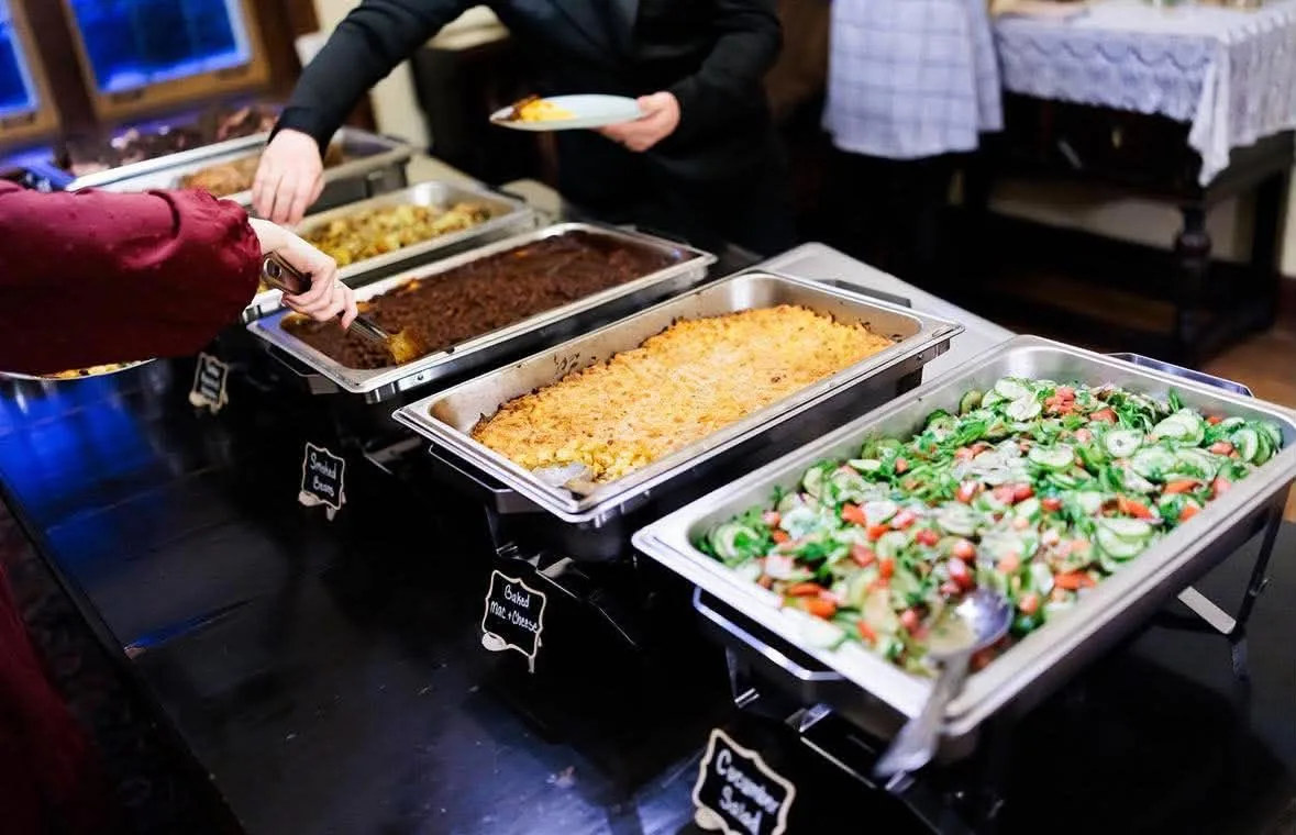 Guests serving themselves from buffet trays of salad and sides.