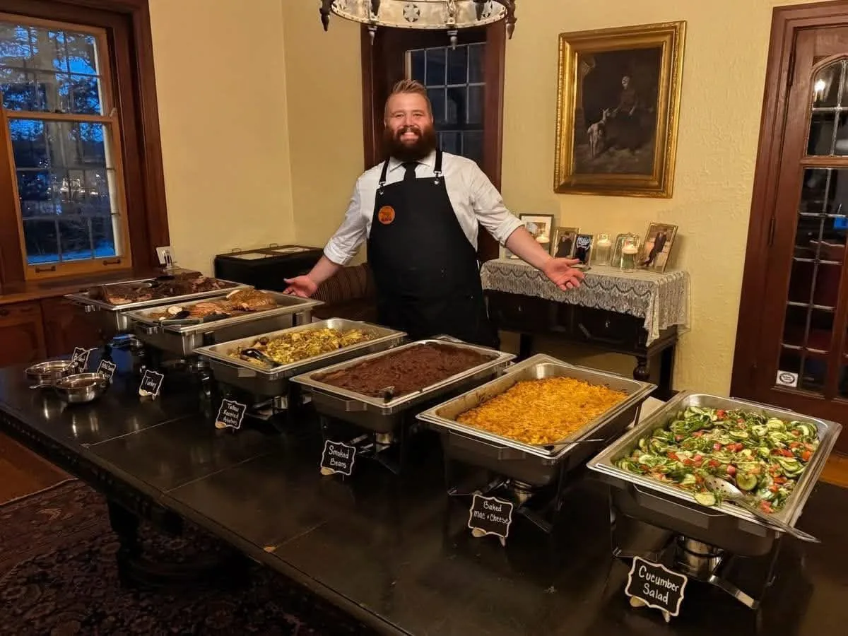 Dalton standing behind a buffet spread of barbecue and sides.