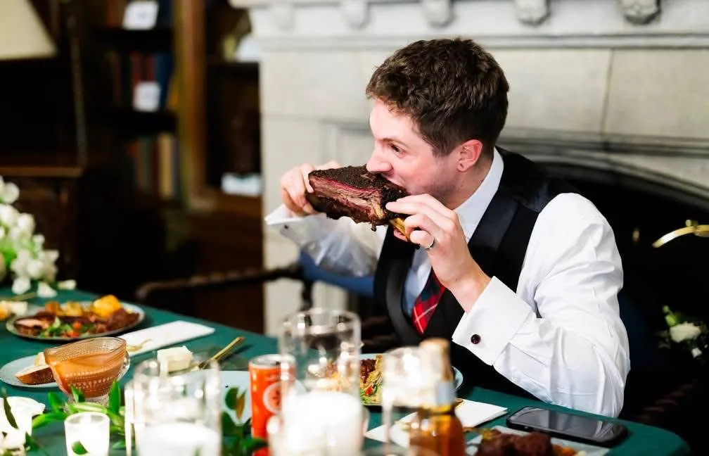 Groom taking a bite of a barbecue rib at the reception table.